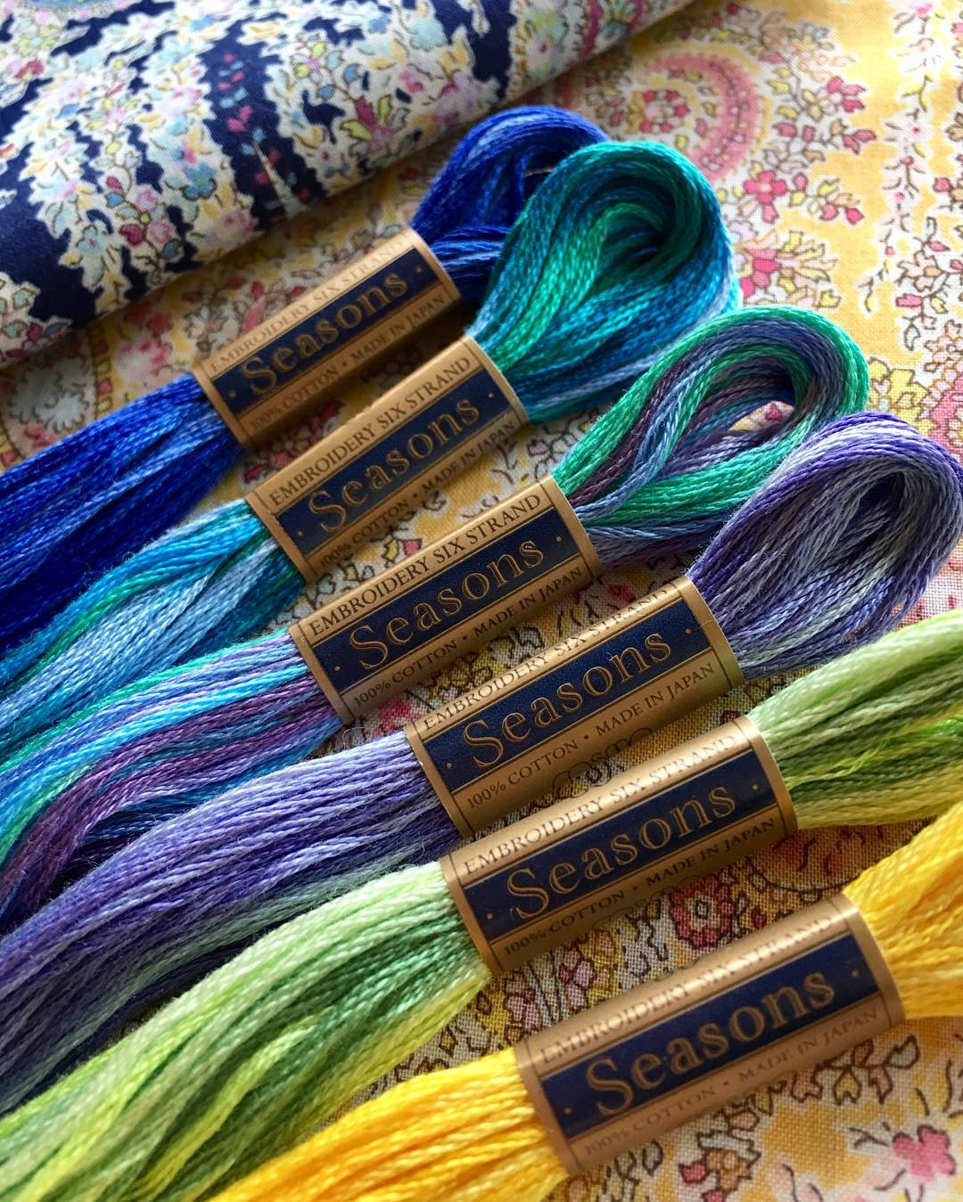 Six COSMO Seasons variegated floss skeins on floral print fabrics