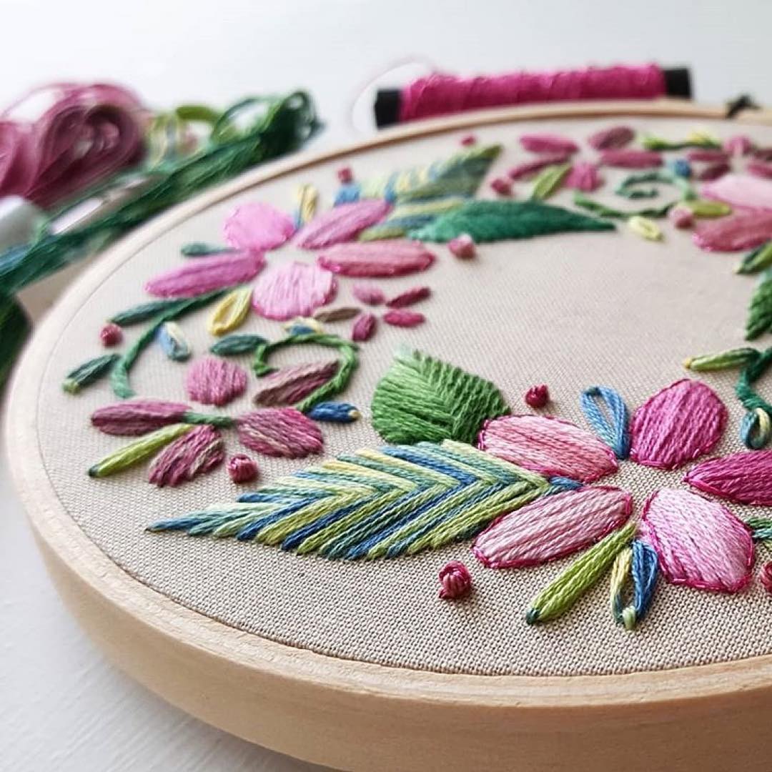 Circular floral wreath embroidery with pink and purple blooms in a wooden hoop
