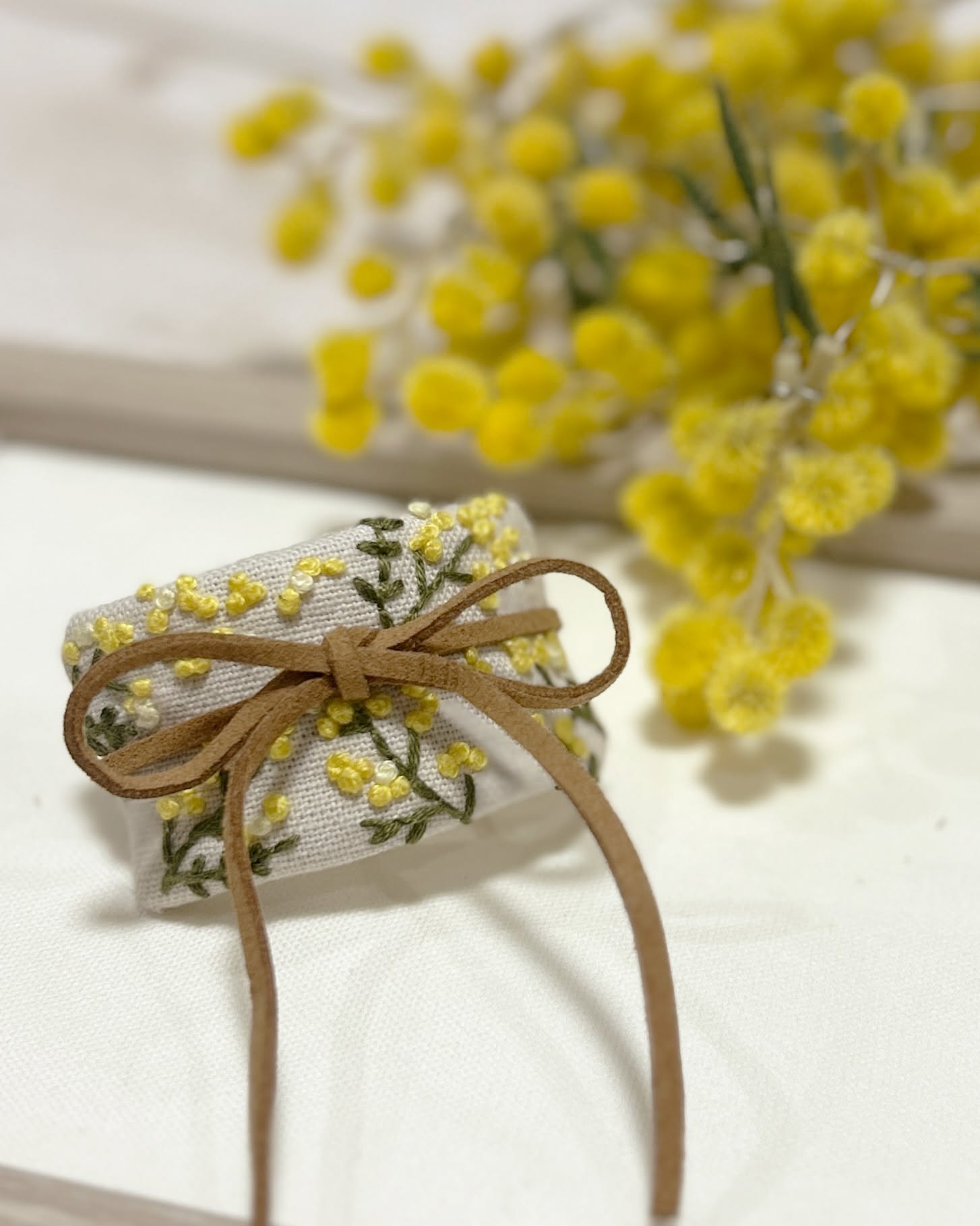 Small linen gift wrap embroidered with yellow mimosa and tied with a brown cord bow