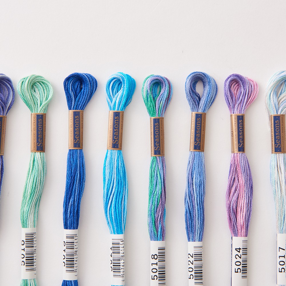 Row of COSMO Seasons variegated floss skeins in blues, greens, and purples