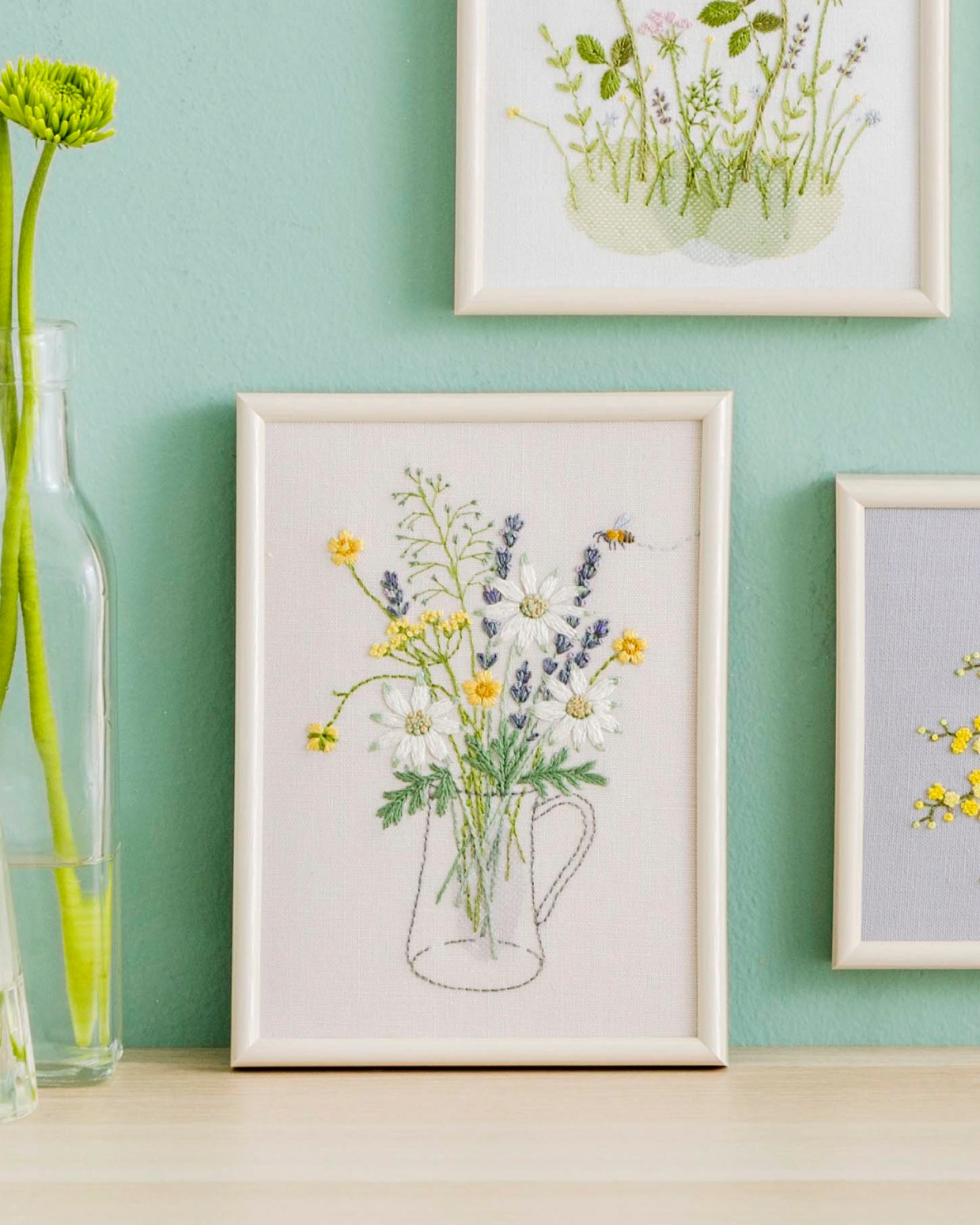 Framed embroidery of a wildflower bouquet in a stitched pitcher outline with a small bee