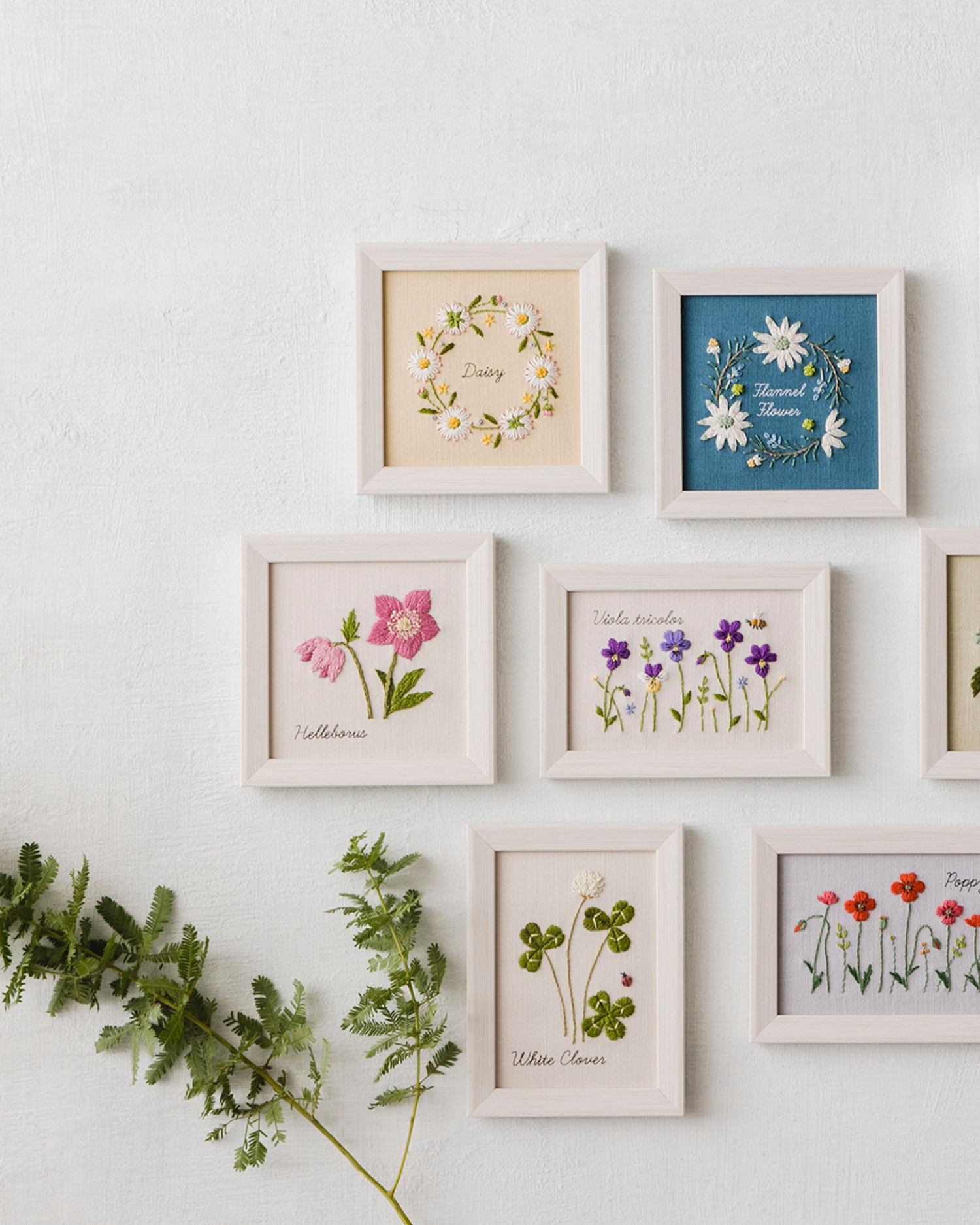 Gallery wall of framed botanical embroideries including daisy, helleborus, viola, clover, and poppy