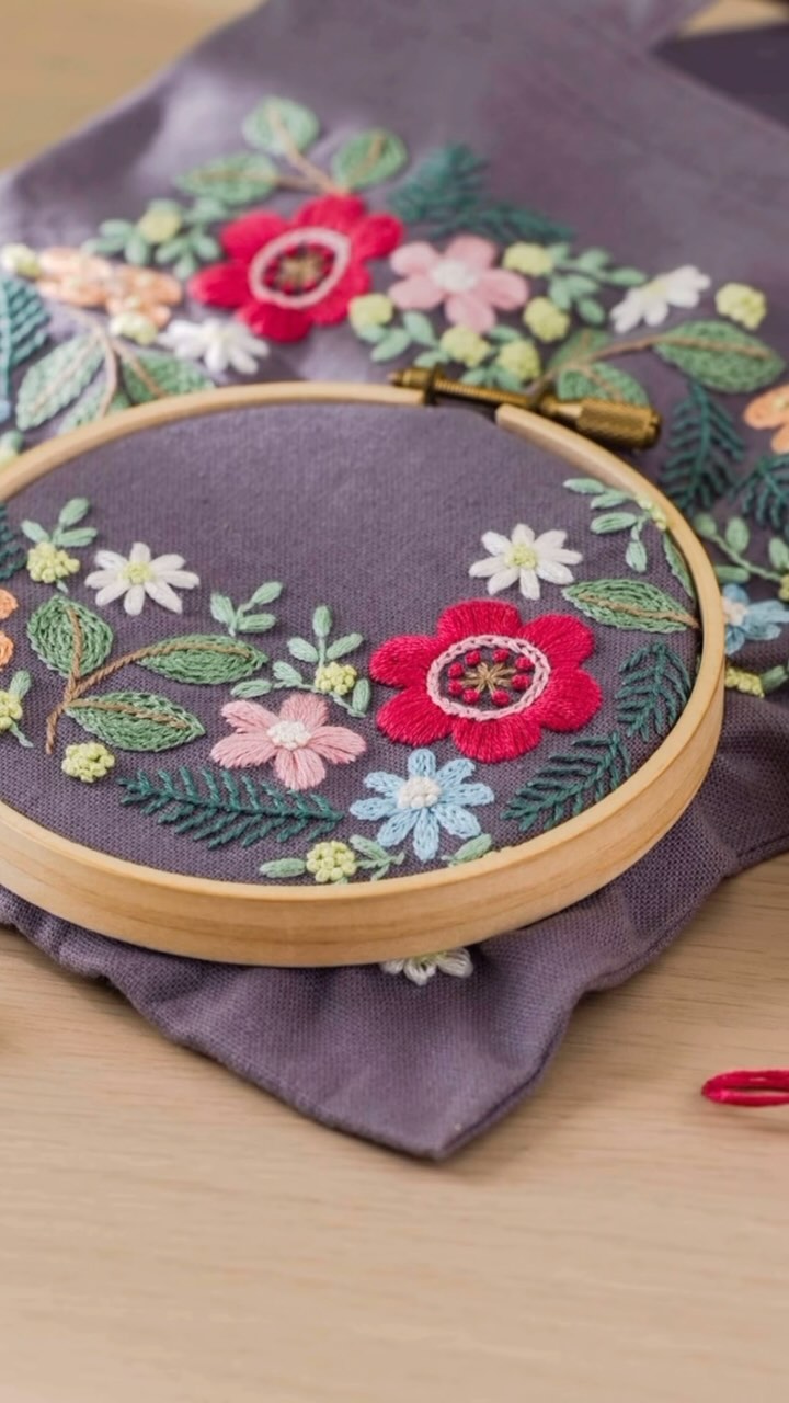 Floral and fern embroidery in a hoop resting on a matching purple embroidered bag