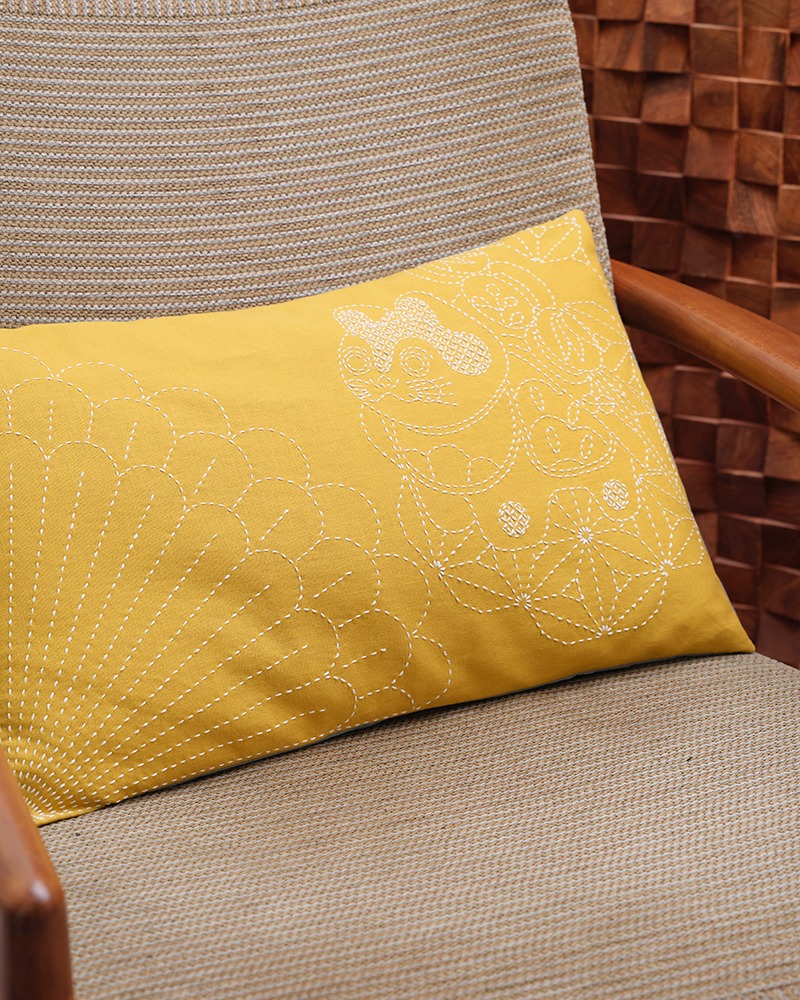 Mustard-yellow pillow with white sashiko fan and geometric motifs on a woven chair